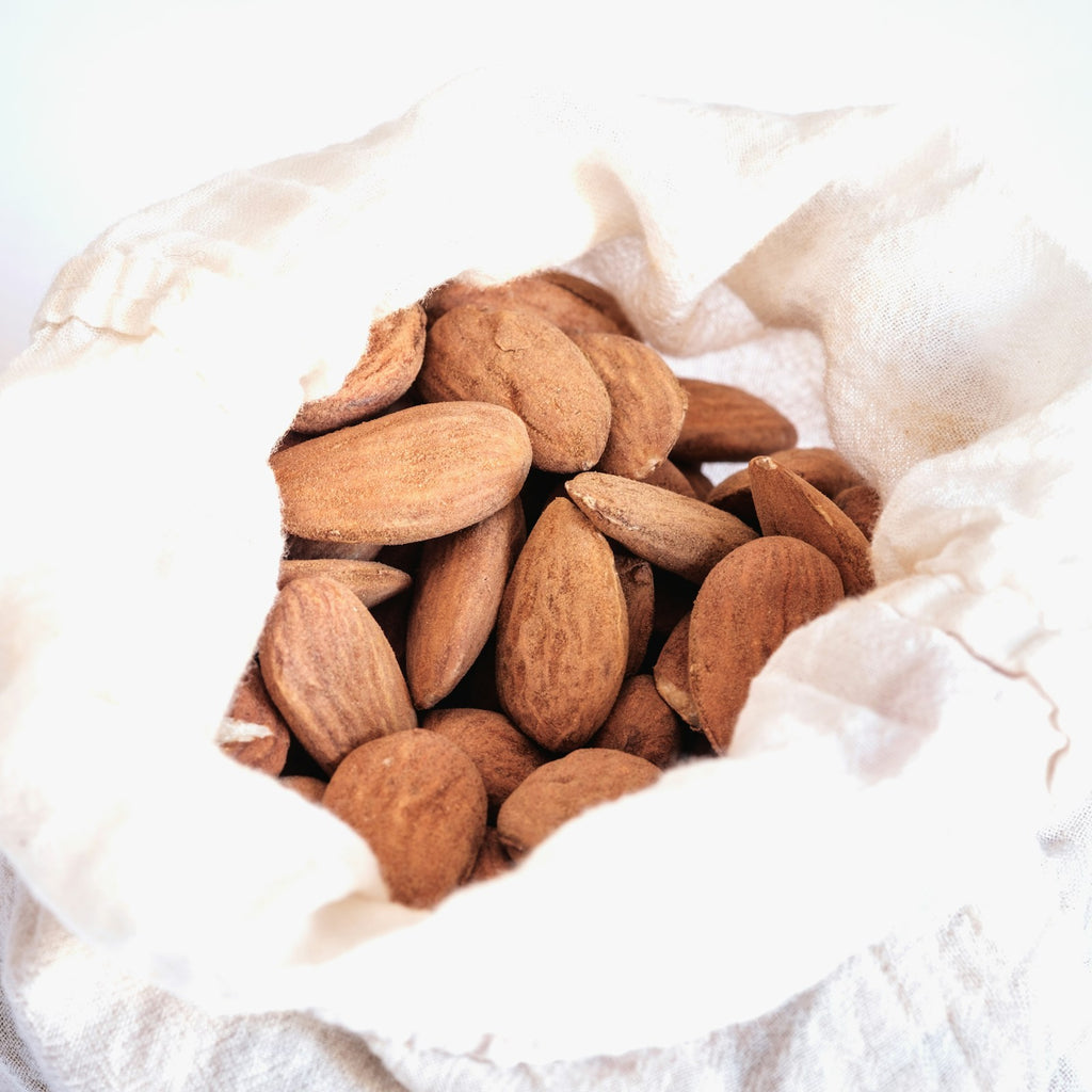 Cotton nut milk bag filled with almonds on a white background