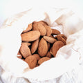 Cotton nut milk bag filled with almonds on a white background