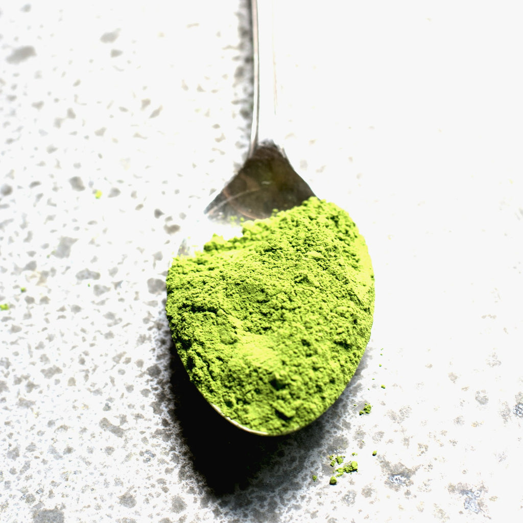 Matcha green tea powder on a spoon against a light background
