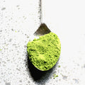 Matcha green tea powder on a spoon against a light background