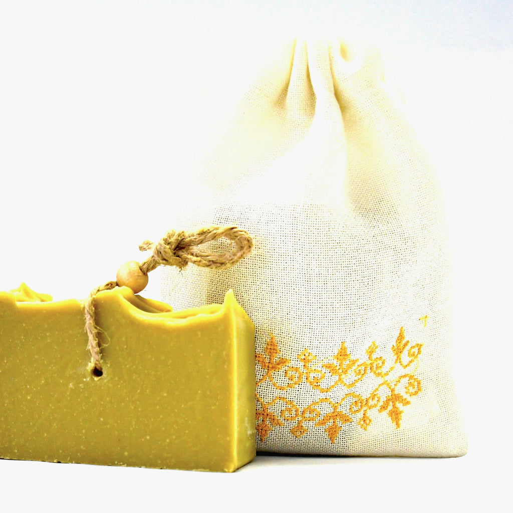 Natural soap bar next to a fabric soap saver pouch on a white background